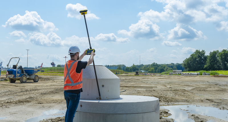 Työntekijä oranssissa turvaliivissä mittaa pisteitä vaikealla alueella Leica CC80 -maastotallentimella ja Leica iCON GPS70:llä.
